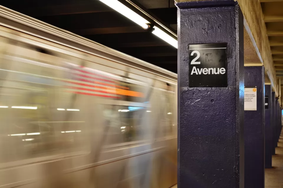 View of 2nd Avenue sign on concrete column on subway platform with blurred train speeding past in New York City.